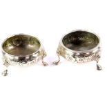 A pair of Georgian matched silver circular salts, embossed with flowers, raised on three cabriole