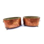 A pair of oval copper planters, with brass lion's head and ring handles, raised on lion's paw