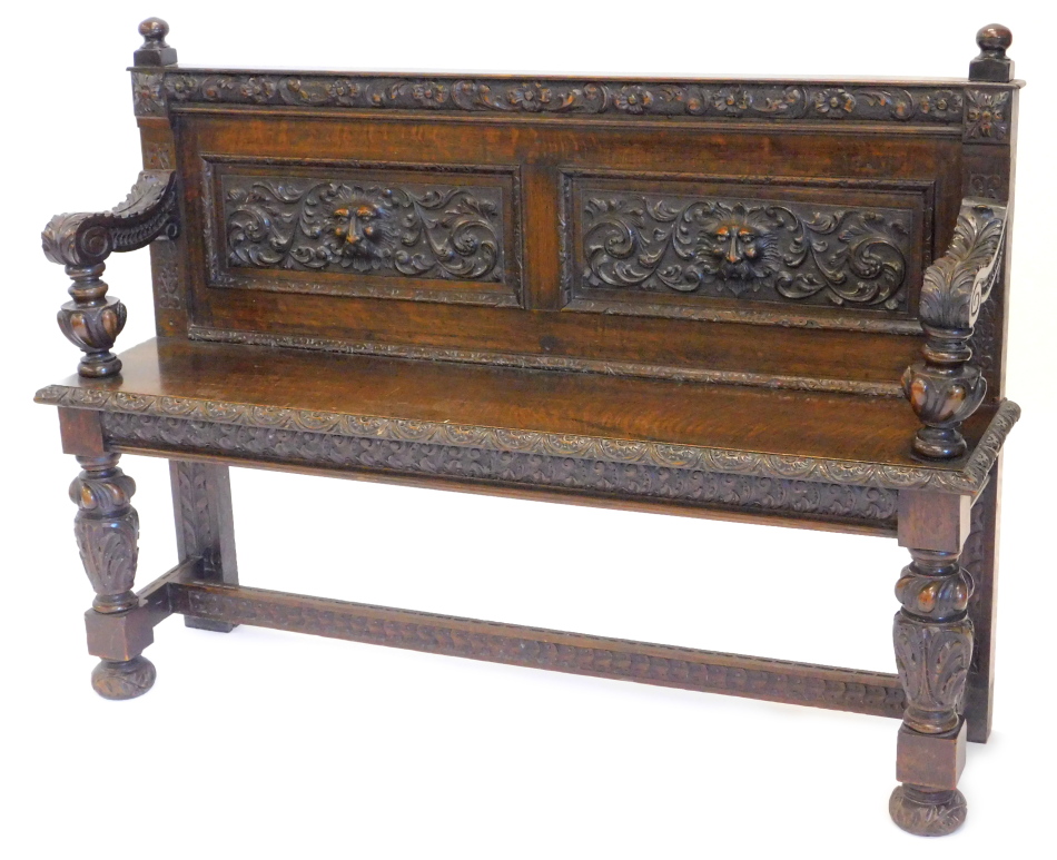 A late Victorian carved oak settle, decorated with leaves, scrolls, flowers and masks, on turned