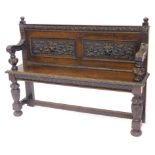 A late Victorian carved oak settle, decorated with leaves, scrolls, flowers and masks, on turned