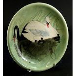 A Moorcroft plaque or plate, decorated with black and white swans with young, on a green ground,