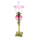 A brass column oil lamp, with cranberry tinted reservoir and shade, 77cm H overall.