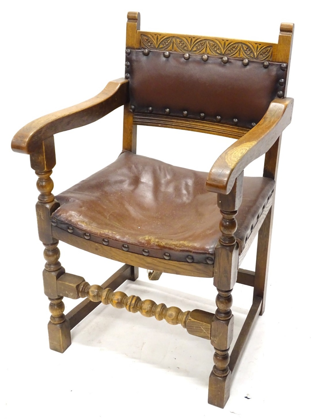 An oak open armchair, with a brown leatherette padded back and seat, on turned legs.
