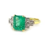An emerald and diamond ring, with central rectangular cut emerald, in yellow gold claw setting,
