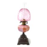 An early 20thC cast iron oil lamp, with a pink honeycomb opaline glass reservoir, with chimney and