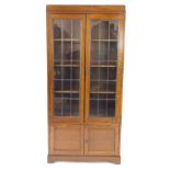 An early 20thC oak cupboard bookcase, with a pair of lead glazed doors opening to reveal three