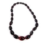 A string of graduated cherry amber beads, twenty three beads, largest 24mm W, 48.2g.