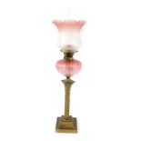 An early 20thC brass Corinthian column oil lamp, with a fluted cranberry glass reservoir, with