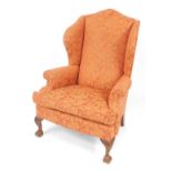 An early Georgian style wingback armchair, upholstered in red and cream floral fabric, raised on