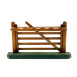 An early 20thC oak pipe rack, formed as a six bar gate, on a green beize covered base, 28cm W.