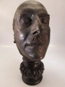 Bronze death mask on carved wooden plinth. Overall height approx 37cm