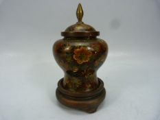 A fine Chinese cloisonne lidded urn in deep reds decorated with flowers with a blue base on a wooden