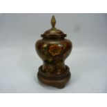 A fine Chinese cloisonne lidded urn in deep reds decorated with flowers with a blue base on a wooden