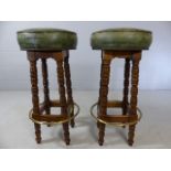 Pair of bar stools with green leather upholstery and brass foot rail