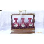 Oak and plated Tantalus inset three cranberry glass bottles,