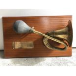 A brass single twist bulb horn mounted on a wooden plaque as The Mercia FM award given by The