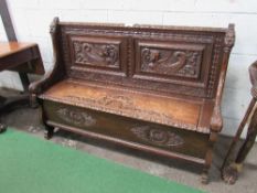 Carved oak settle with rising seat to storage, 137cms x 45cms x 97cms. Estimate £200-250.