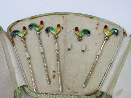 A case containing 4 silver cocktail sticks with colourful enamel cockerels, plus another enamel