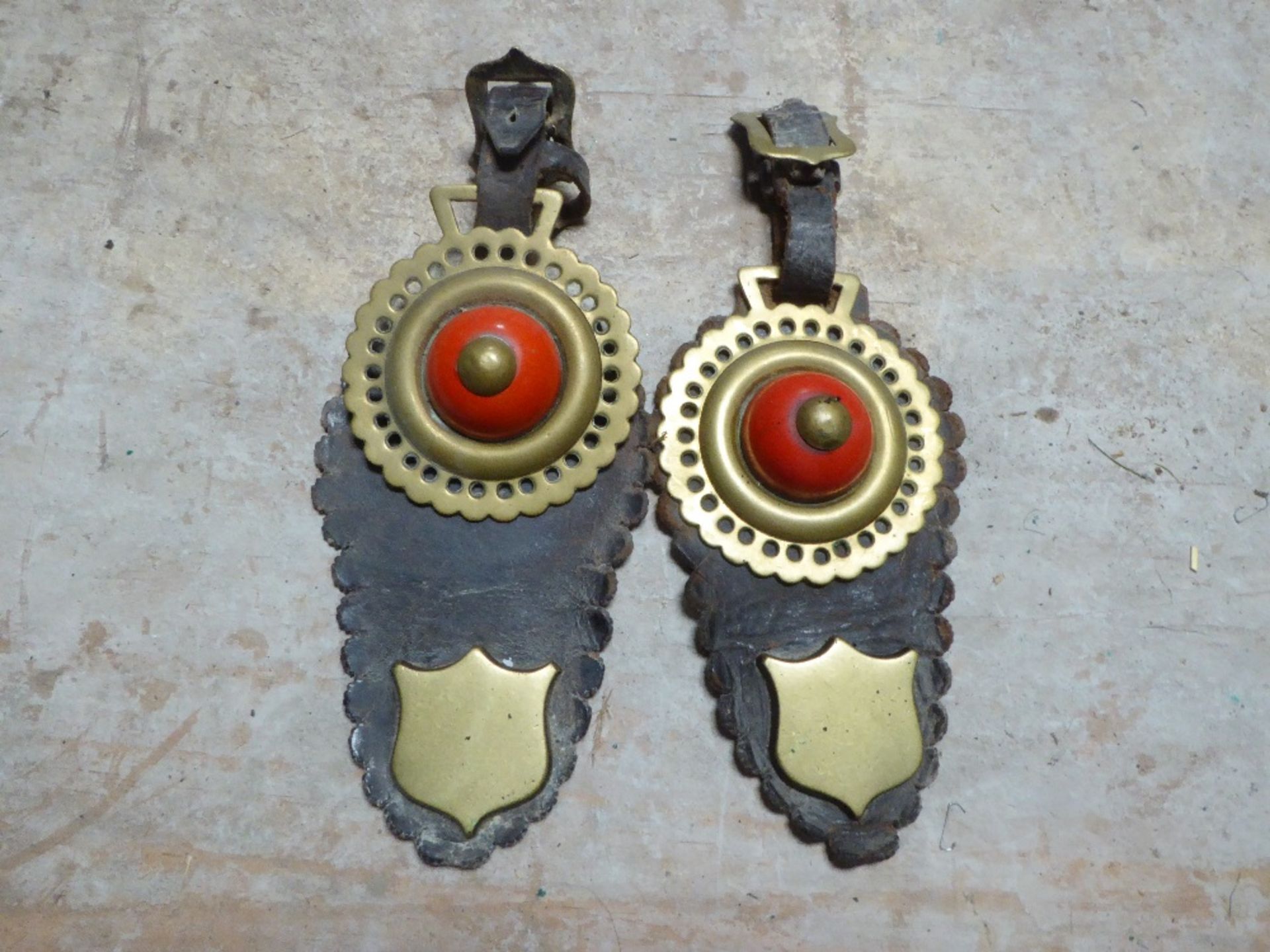 Pair of shaped leather headpieces each with a horse brass with red ceramic boss, shield stud and