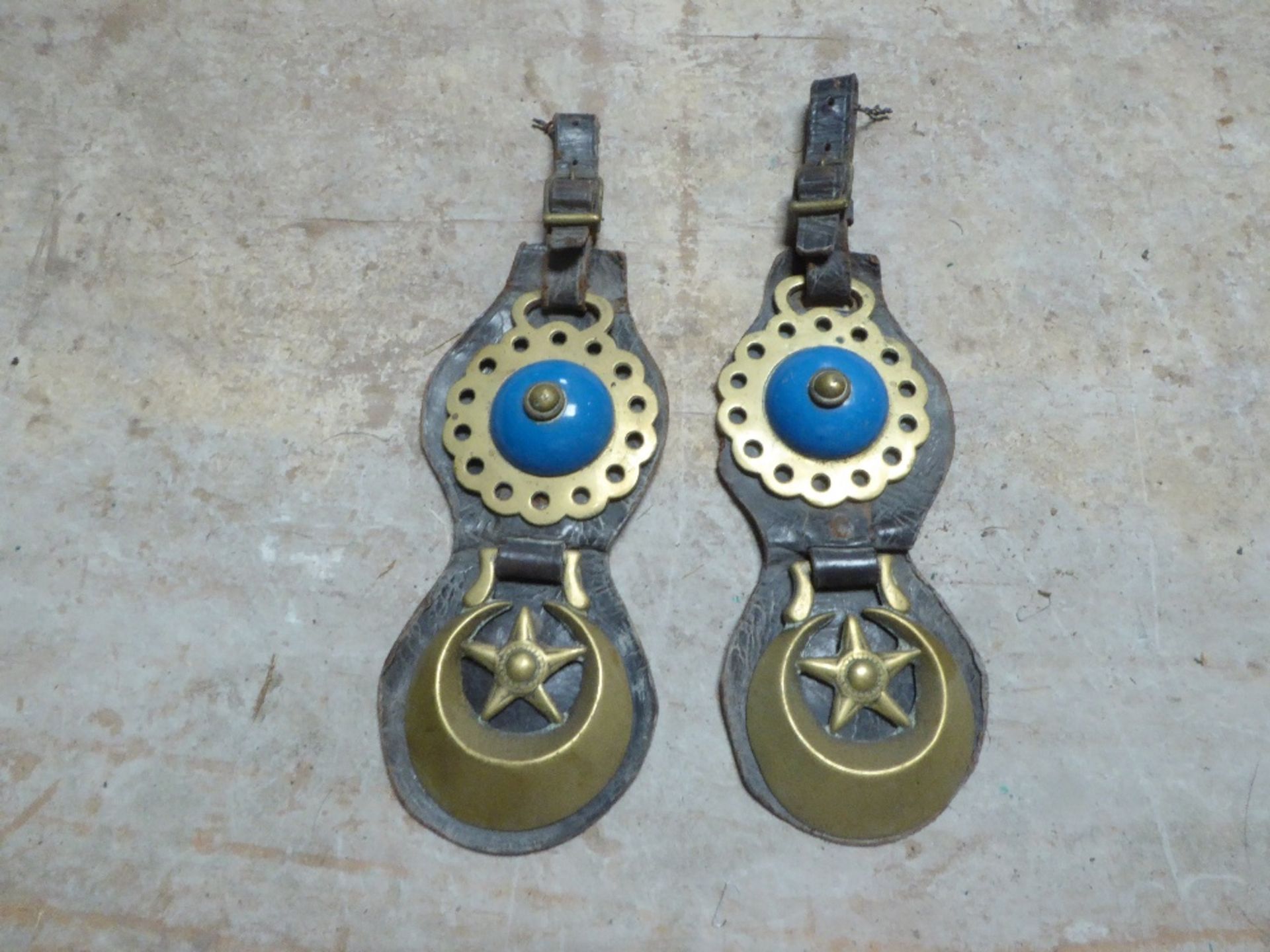 Pair of shaped leather headpieces each with a star centre crescent brass and another with a blue