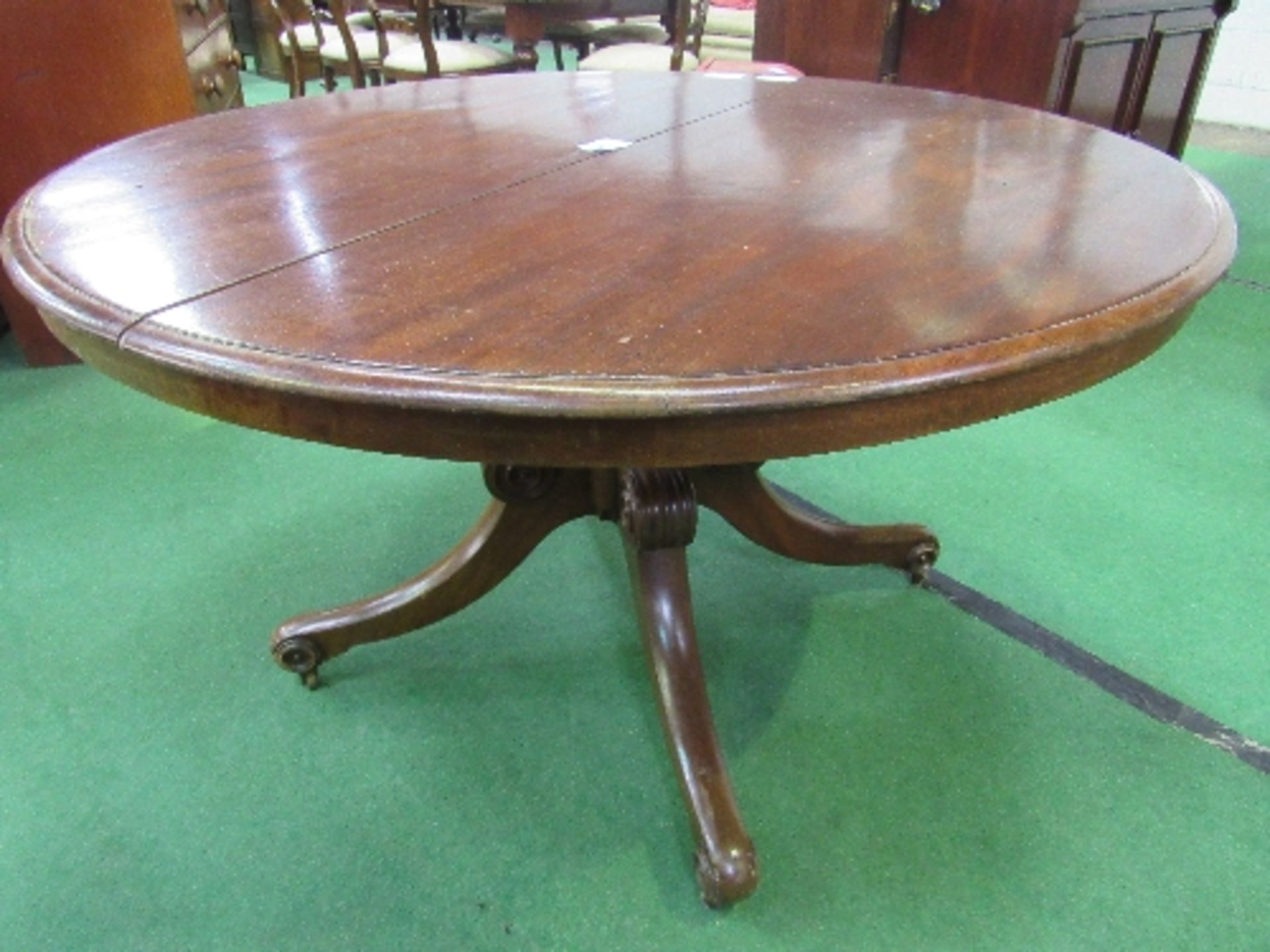 Mahogany circular tilt-top table on heavy turned column to 3 scrolled feet with caster, 122cms