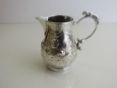 Small silver coloured metal jug, repousse decorated with fruit & leaves with a small dog figurine to