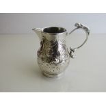 Small silver coloured metal jug, repousse decorated with fruit & leaves with a small dog figurine to