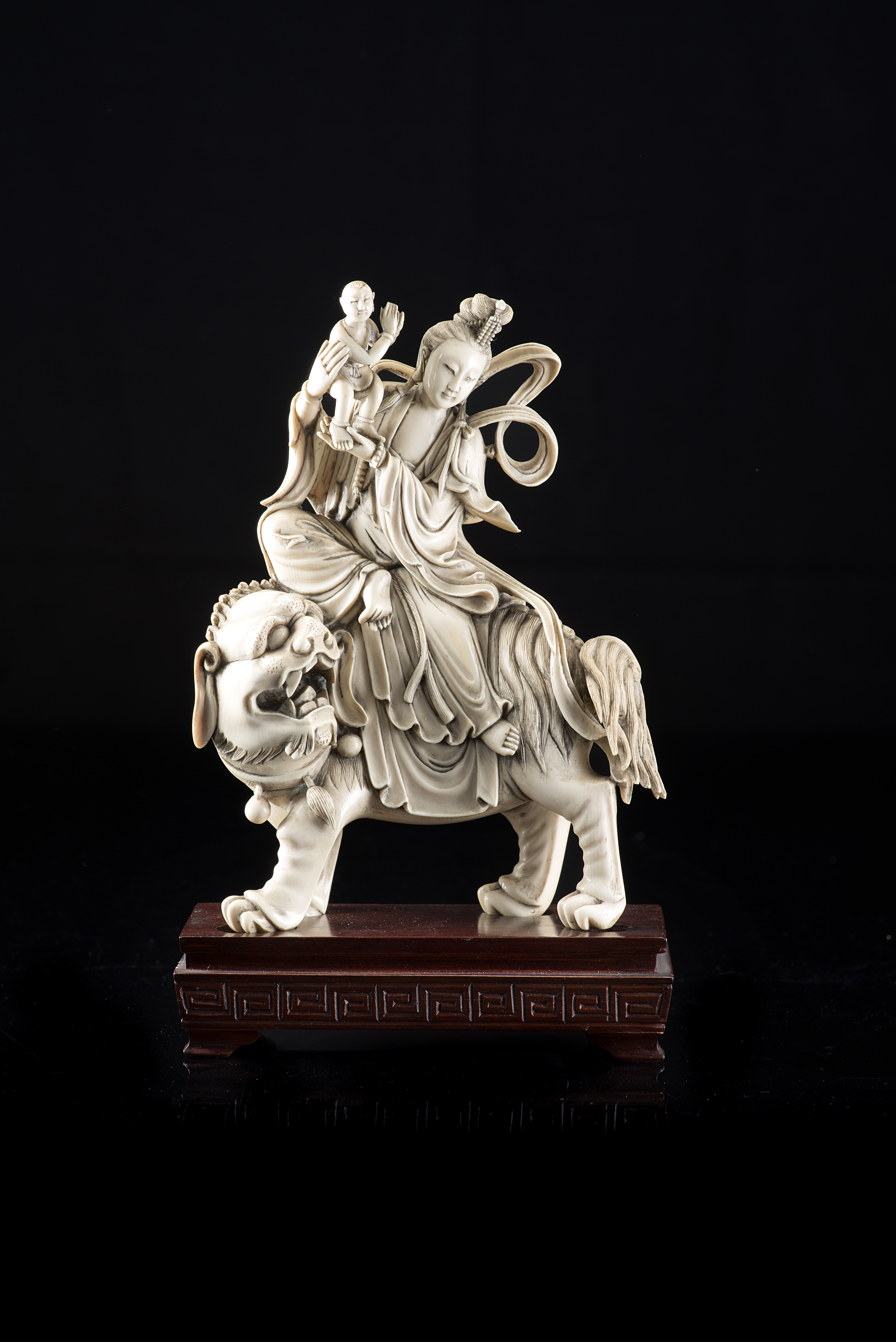 An ivory sculpture depicting Guanyin on a Buddhist lion, wood base (slight defects)China, early 20th