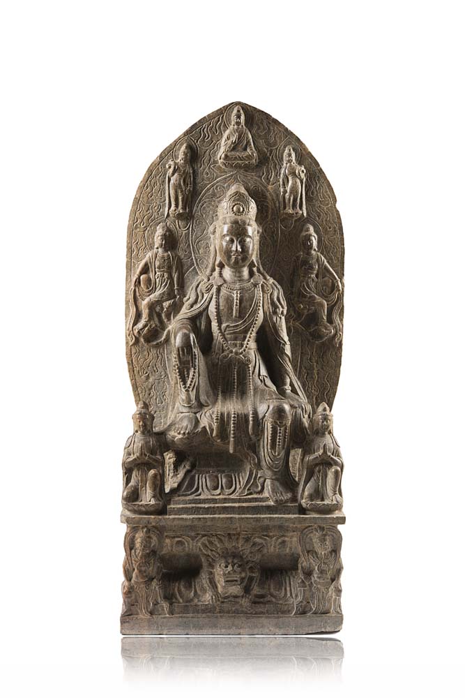 A grey stone stele carved with a seated Guanyin wearing long robes, the mandorla with more