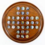 A mahogany solitaire board with 33 German pontilled glass swirl marbles 16 to 18 mm, board diameter