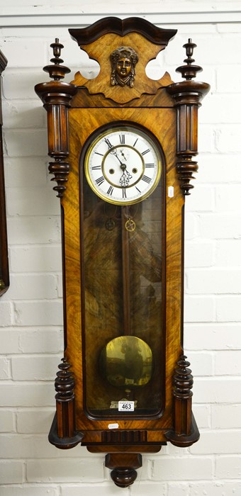 A walnut cased Viennese style wall clock with mask pediment.