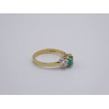 An 18ct yellow gold ring set with a dahlia cut Emerald flanked by two diamonds, 3g,