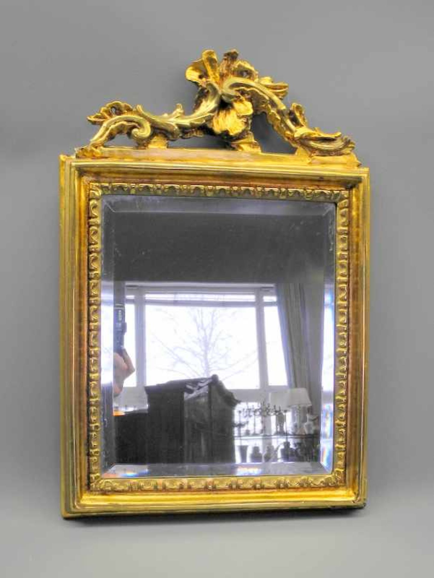 Kompakter WandspiegelHolz geschnitzt, goldfarben bemalt/Spiegelglas. Rehteckiger Spiegel mit