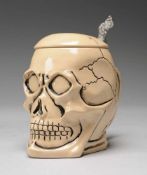 Totenkopf-BierkrugSteingut. Krug in Form eines auf Knochen liegenden Schädels. Griff in Knochenform.
