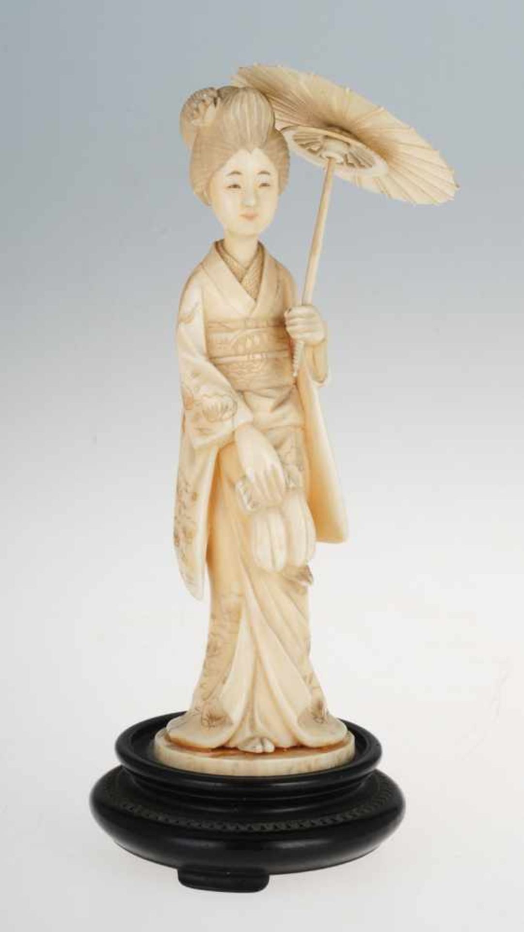 Okimono einer GeishaBein. Auf rundem geschwärzten Holzsockel Darstellung einer jungen Frau, einen