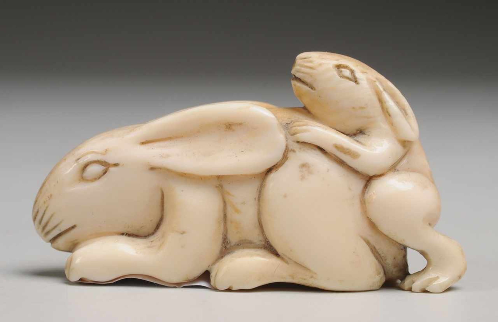 NetsukeElfenbein, geschnitzt. Plastische Darstellung eines Hasenpaares. Geschwärzter Gravurdekor.
