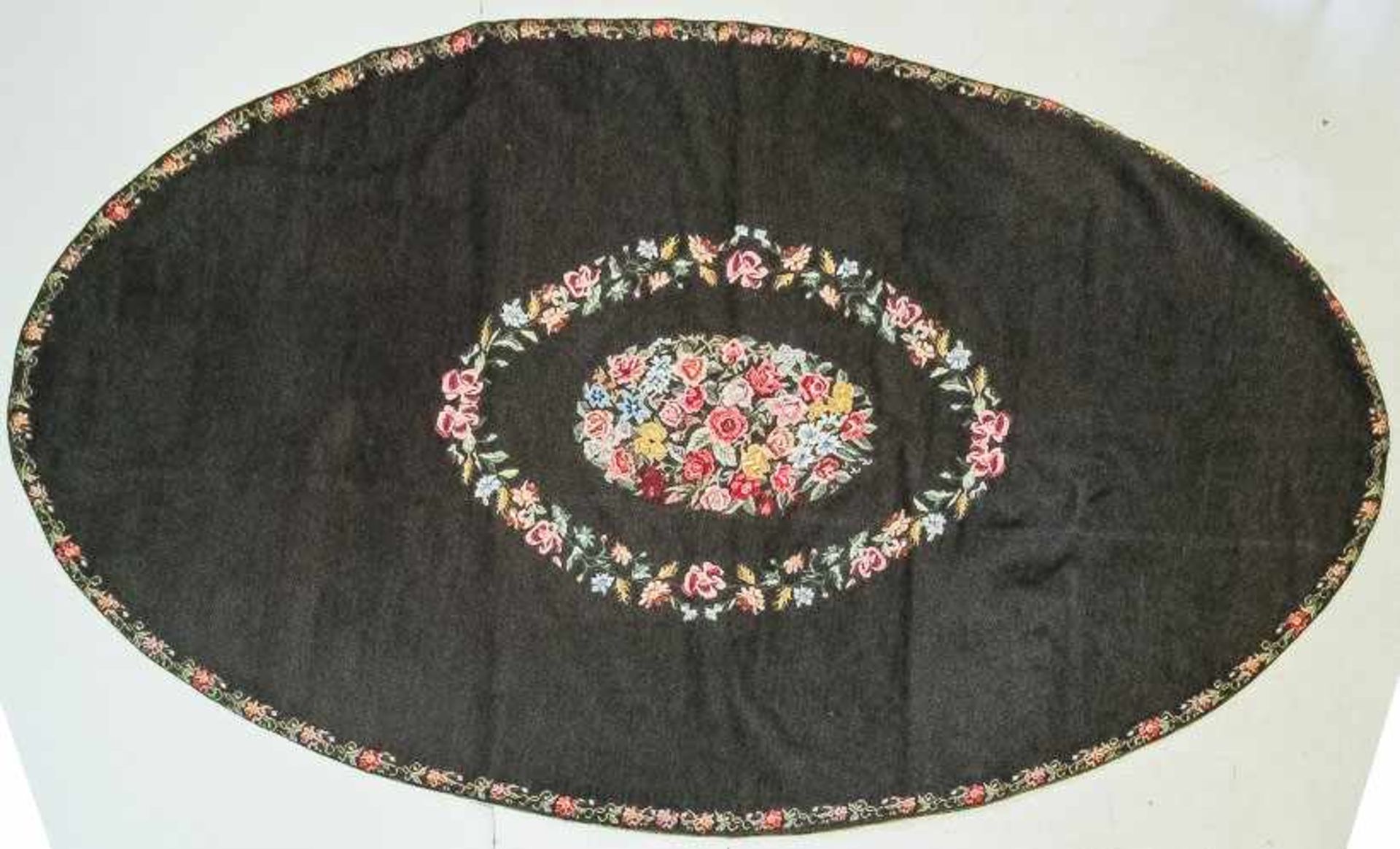 Ovale Deckemit bunter Gros-Point-Stickerei auf schwarzem Grund. Leuchtender Blumendekor aus