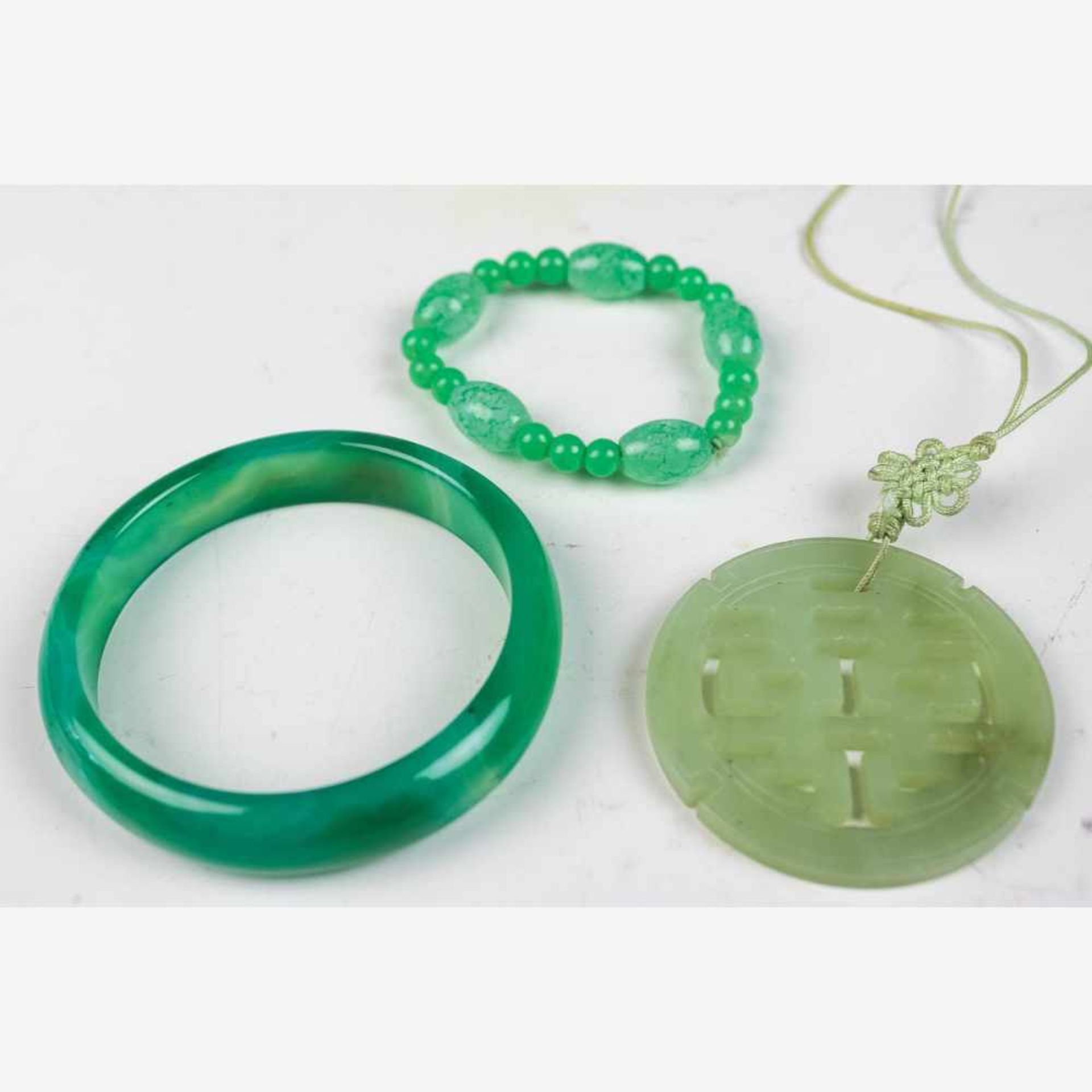 Armreif, Armband u. runder AnhängerChinaGrüne bzw. weißliche Jade. a) D. 7 cm. b) Kl. Perlen u.