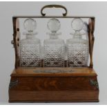 Oak three decanter tantalus, with brass mounts & sectionalised drawer beneath, patent stamp to brass