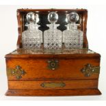 Tantalus. Oak tantalus with three cut glass decanters, brass mounts, height 34.5cm, width 34cm depth