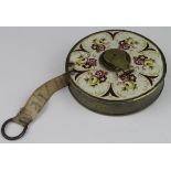 Tape Measure. A brass cased 40ft cloth tape measure, with floral enamel decoration to one side of