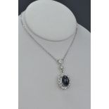 A beautiful sapphire and diamond set oval shaped cluster pendant with a central oval cabochon cut sa