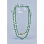A string of 100 ungraduated pale green Jade Beads in a necklace with gold metal clasps.