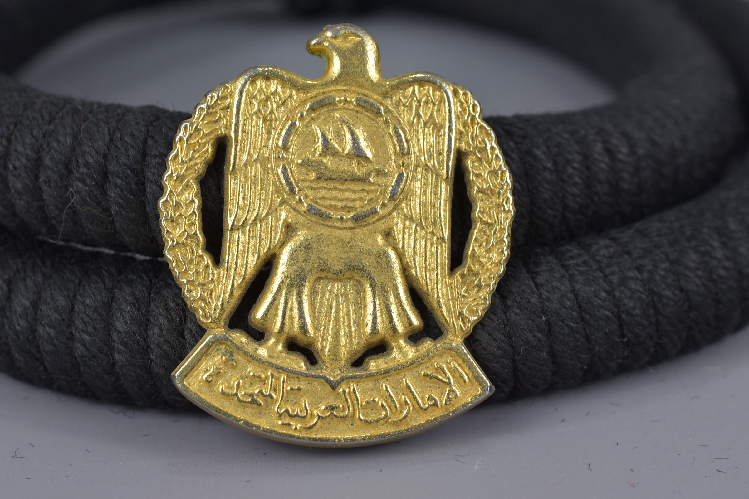 An Islamic braided rope belt and headband fitted with a metal badge of arms with inscription - Image 2 of 2