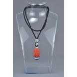 A carved coral Buddha head pendant with a banded agate on a string.