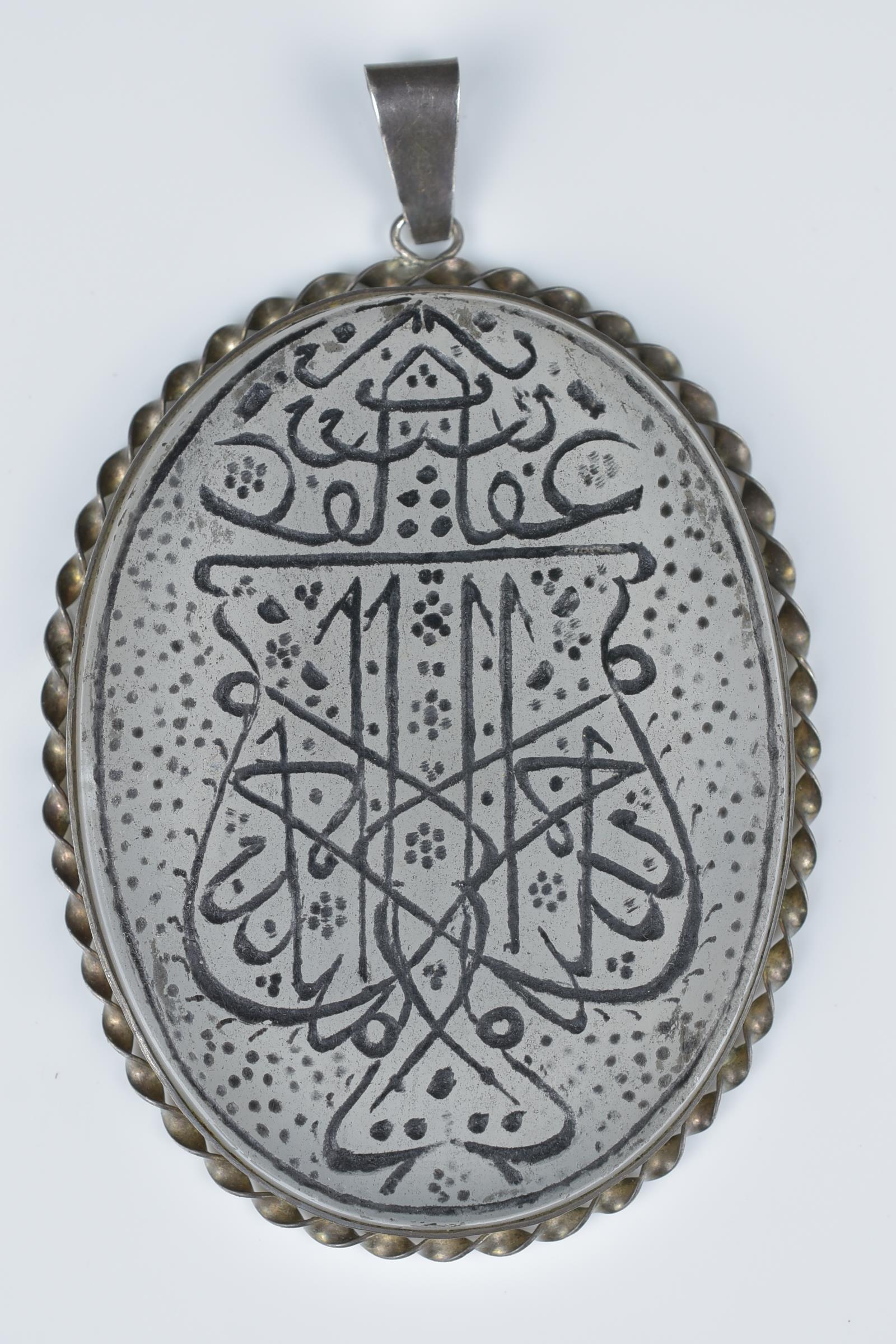A Persian white metal pendant with inscription.