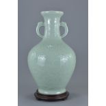 A Chinese celadon porcelain twin handle vase attached to wooden stand. Hole through centre of vase b