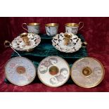A set of three brass cups and saucers painted with enamel decoration, with two candle holders.