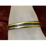 A 14k gold bangle set with 24 emeralds of baguette cut.