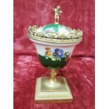 A beautifully painted ceramic urn with lid mounted on a brass plinth.